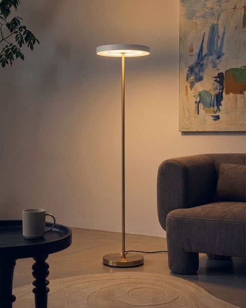 Moderne LED Stehlampe mit rundem Leuchtkopf und schlankem Metallständer in Wohnzimmer mit Sessel und Beistelltisch.