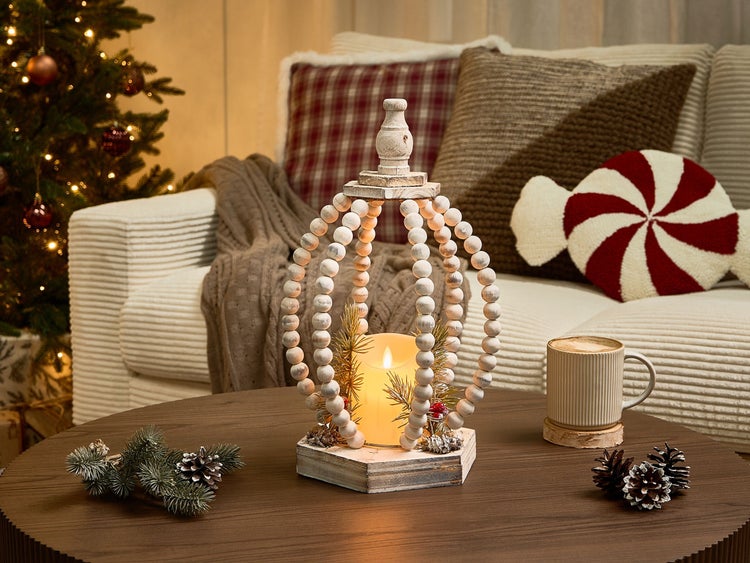 Dekorative Tischszene mit LED Kerze in Holzlaterne, Tasse Kaffee und Weihnachtsbaum im Hintergrund