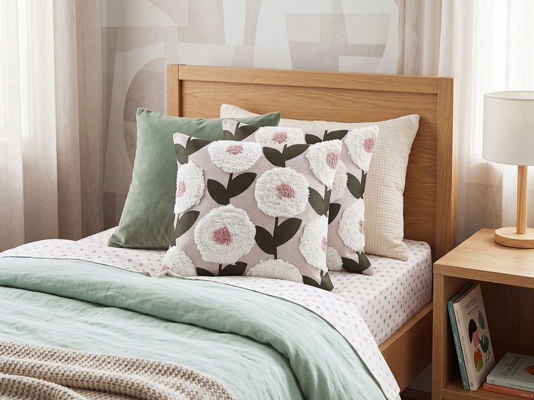 Dekokissen mit Blumenmuster auf einem Doppelbett mit Holzgestell in einem modern eingerichteten Schlafzimmer mit weiteren Wohntextilien.
