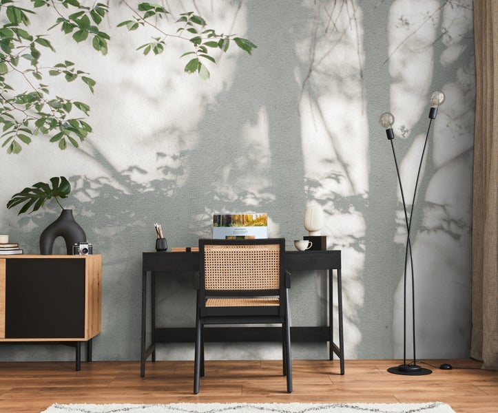 Fototapete mit Schattenwurf von Blättern und Zweigen in einem hellen Arbeitszimmer mit schwarzem Schreibtisch und Wiener Geflecht Stuhl.