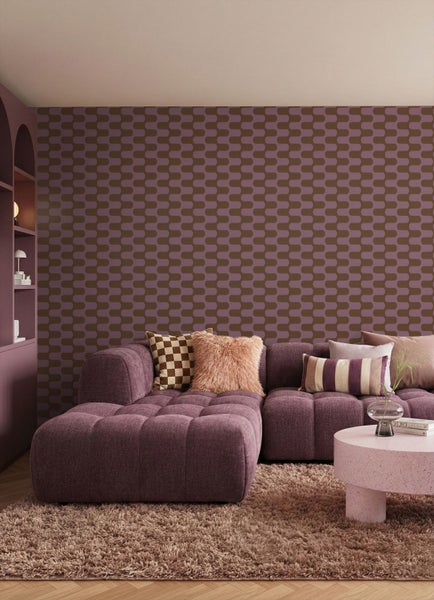 Modernes Wohnzimmer mit geometrisch gemusterter Vliestapete, lila Modulsofa, Hochflor-Teppich und rundem Couchtisch.