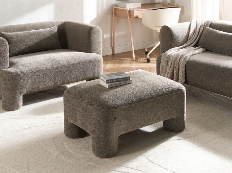 Moderner Wohnbereich mit Hocker aus strukturiertem Stoff, passenden Sesseln und einem Holzschreibtisch in einem hellen, organisierten Raum.