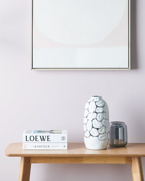 Dekoratives Arrangement mit Vasen und Büchern auf einem Holztisch vor einer Wand mit einem gerahmten Bild