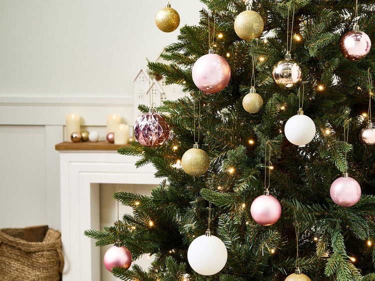 Weihnachtsbaum geschmückt mit rosa, weißen und goldfarbenen Kugeln sowie warmweißen Lichtern. Helles Zimmer mit Kamingesims und Kerzen.