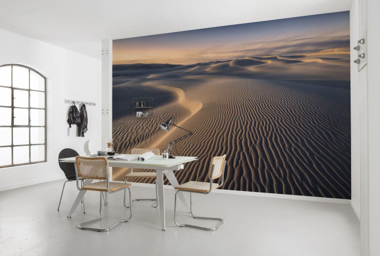 Ein Zimmer mit einer Fototapete, die eine Sanddünenlandschaft zeigt, mit Esstisch und Stühlen.