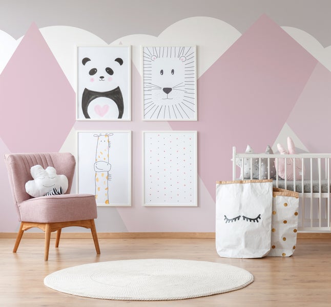 Modernes Babyzimmer mit geometrischer Wandgestaltung, rosafarbenem Sessel, weißem Kinderbett, Tierbildern und rundem Teppich.