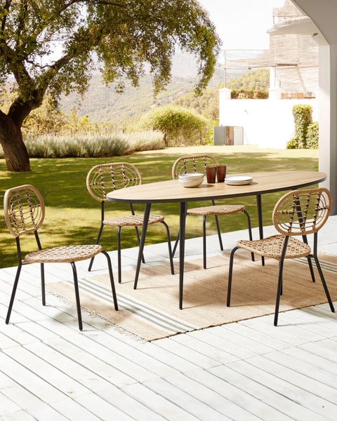 Gartenszene mit ovalem Tisch und vier Stühlen mit Rattanbespannung auf einem Teppich