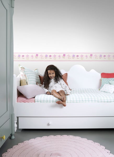Dekoriertes Kinderzimmer mit Mädchen, Bett, Blumentapete und rundem Teppich