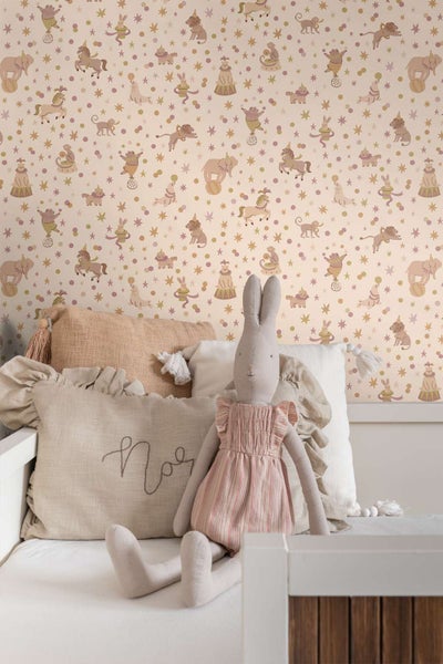 Kindertapete mit Zirkusmotiven wie Tieren und Sternen in einem Kinderzimmer mit weichen Kissen und einer Stoffhasenpuppe auf einem Bett.