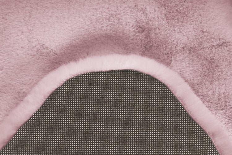 Nahaufnahme eines rosa Kunstfellteppichs mit weicher Plüschoberfläche und rutschfester Rückseite mit Noppen.
