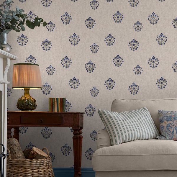 Wohnzimmer mit beiger Mustertapete mit blau-goldenen Ornamenten, eingerichtet mit Sofa, Holzkonsole und einer Tischleuchte.