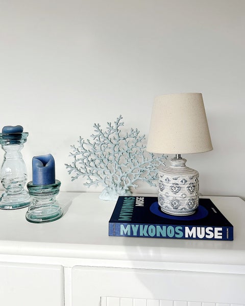 Dekoratives Stillleben mit Tischlampe, Koralle, Kerzen und Kerzenhaltern auf einem weißen Tisch.