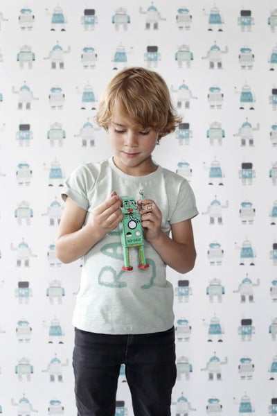 Junge hält Spielzeugroboter vor Tapete mit Robotermuster