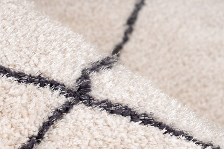 Nahaufnahme eines hellen Hochflor-Teppichs mit dunklem Rautenmuster und weicher Struktur.