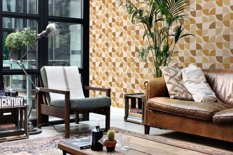 Wohnzimmer mit geometrischer Tapete mit Kreisen in Ocker und Beige. Heller Raum im Industriestil mit Ledersofa und Holzarmlehnsessel.