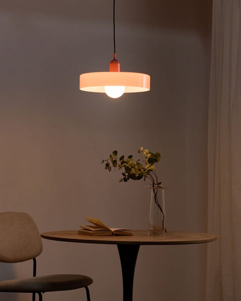Hängeleuchte mit rundem Schirm über einem Holztisch mit Buch und Vase in einem gemütlich beleuchteten Raum.
