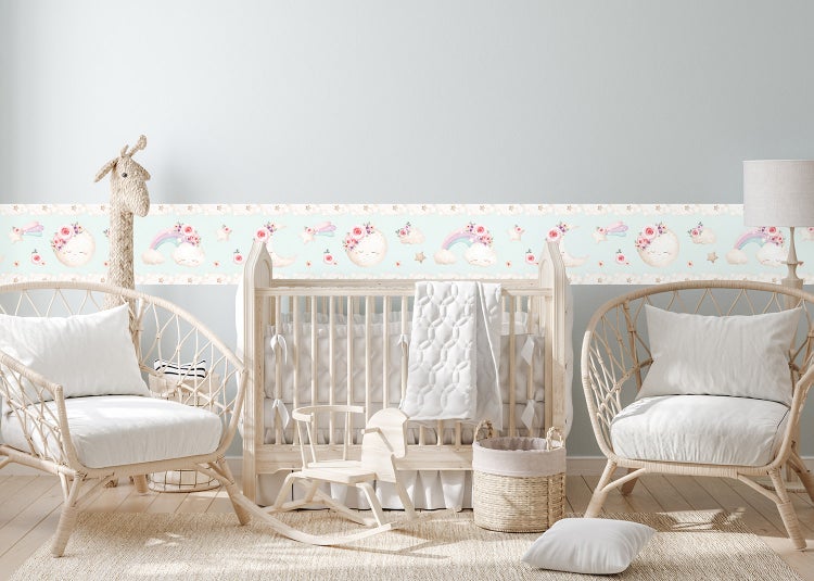 Selbstklebende Tapetenbordüre für das Kinderzimmer mit Motiven von Mond, Sternen und Regenbogen an einer Wand über einem Tisch mit zwei Stühlen.