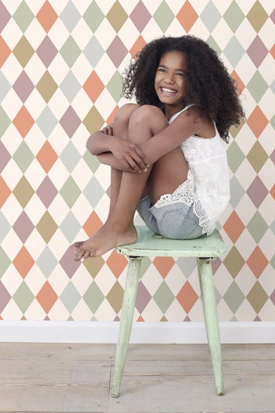 Mädchen sitzt auf einem Hocker vor einer Wand mit Rautenmuster