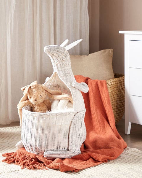 Weißer Aufbewahrungskorb aus geflochtenem Material in Känguru-Form in einem hellen Kinderzimmer mit Plüschtier und Wohndecken.