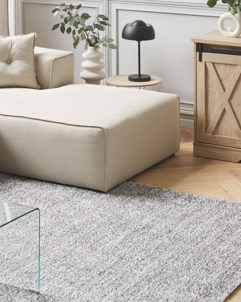 Wohnzimmer mit beigem Sofa, Couchtisch aus Glas und Teppich