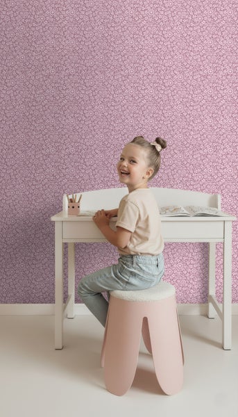 Mädchen sitzt an einem Schreibtisch vor einer floral gemusterten Tapete