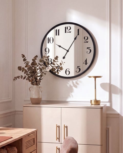 Große runde Wanduhr mit Zifferblatt hinter Glas, montiert über einem modernen Sideboard mit Vase und Tischlampe im eleganten Wohnbereich.