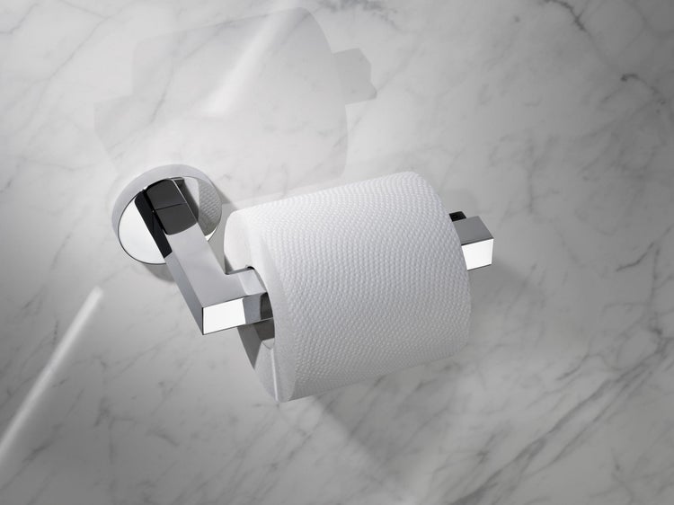 Wandmontierter Toilettenpapierhalter aus Metall mit glänzender Oberfläche montiert an einer hellen Marmorwand mit einer Rolle Toilettenpapier.