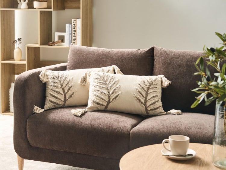 Wohnzimmer mit braunem Sofa, Zierkissen mit Blattmuster und Holzregal