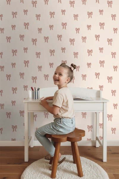 Mädchen sitzt an einem weißen Schreibtisch vor einer Wand mit Schleifenmuster