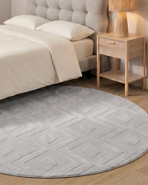 Runder Teppich mit geometrischem Rautenmuster in einem modern eingerichteten Schlafzimmer neben einem Holznachttisch und einem Bett.