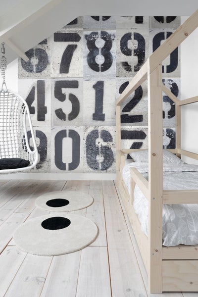 Kinderzimmer mit Holzbett, Hängesessel, runden Teppichen und Fototapete mit Zahlenmotiven.