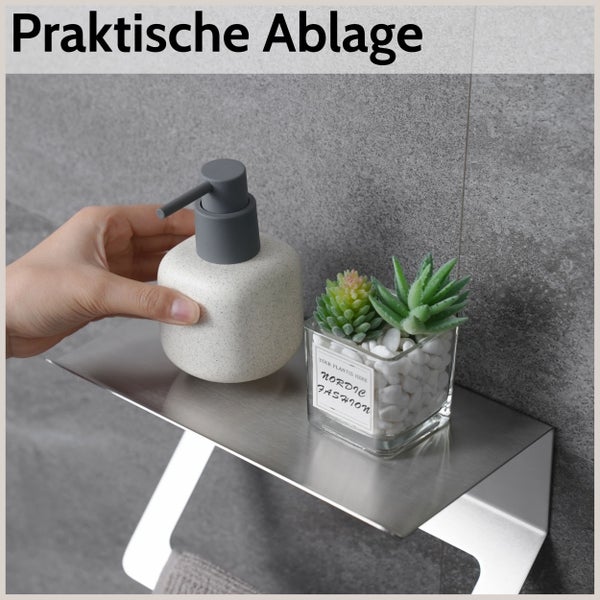 Wandmontierte Ablage aus Edelstahl im Badezimmer mit einem Seifenspender und einer kleinen dekorativen Pflanze.