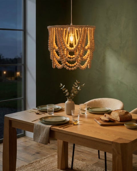 Pendelleuchte mit Schirm aus natürlichen Holzperlen über einem gedeckten Esstisch aus Holz vor einer grünen Wand.