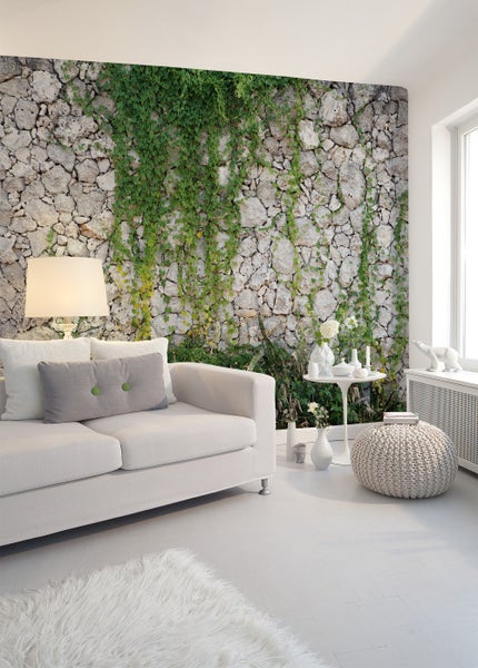 Fototapete mit Steinmauer-Optik und grünem Efeu in einem hellen, modern eingerichteten Wohnzimmer mit Sofa und Beistelltisch.