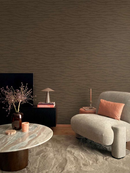 Wohnzimmer mit dunkler Vliestapete mit feinem, organischem Wellenmuster, kombiniert mit modernen Möbeln und Wohnaccessoires.