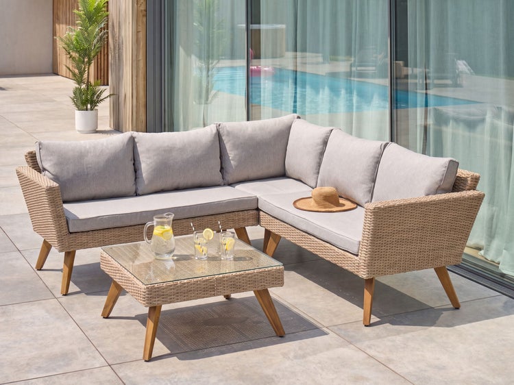 Lounge-Set bestehend aus Ecksofa und Couchtisch in Geflecht-Optik mit grauen Kissen und Holzbeinen auf einer Terrasse.