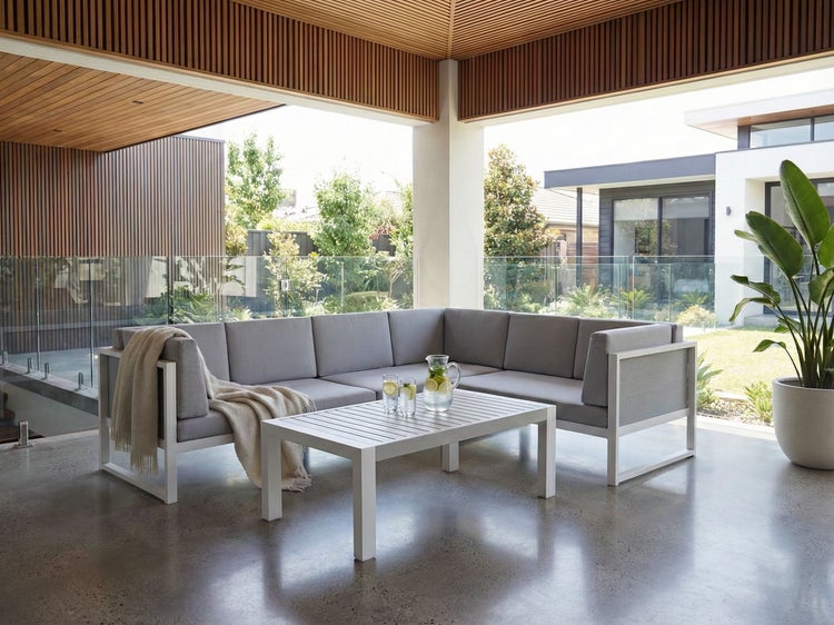 Helle Terrasse mit grauer Eckcouch, weißem Tisch, Getränken und Zimmerpflanze