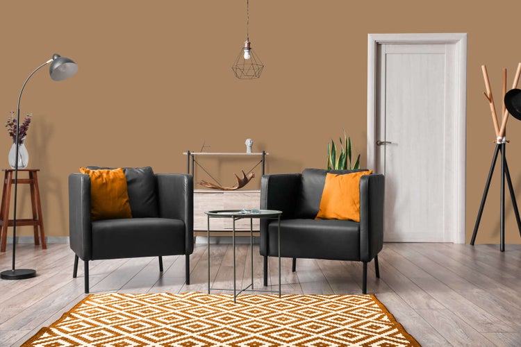 Modernes Wohnzimmer mit ockerfarbener Wandfarbe, zwei schwarzen Sesseln mit orangefarbenen Kissen und einem gemusterten Teppich auf Holzboden.