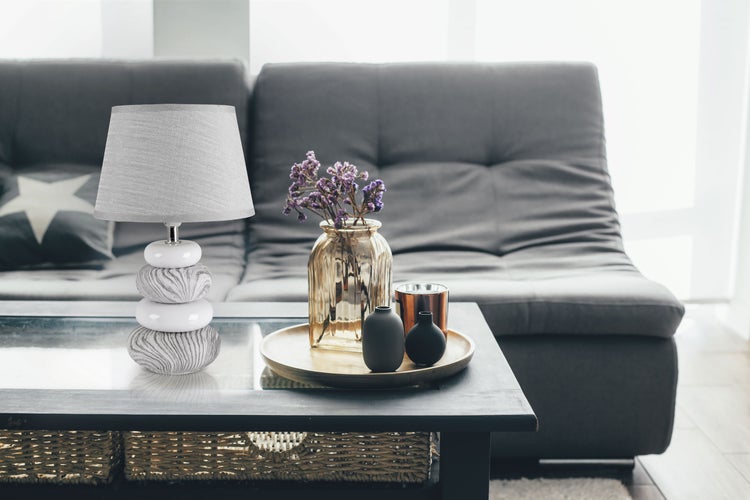 Dekorative Tischszene mit Lampe, Blumen und Vasen auf einem Tisch vor einem Sofa