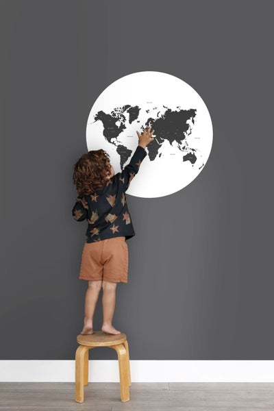 Kind steht auf einem Hocker und berührt eine Weltkarte an der Wand
