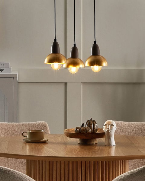 Szene mit drei Pendelleuchten über einem Esstisch, dekoriert mit Kürbissen und einer Kopfskulptur.