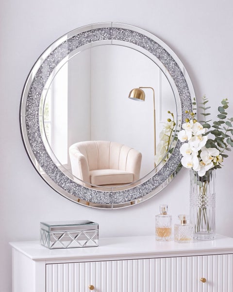 Runder Wandspiegel mit facettiertem Rahmen mit Glitzersteindekor über einer weißen Kommode mit Dekoration.