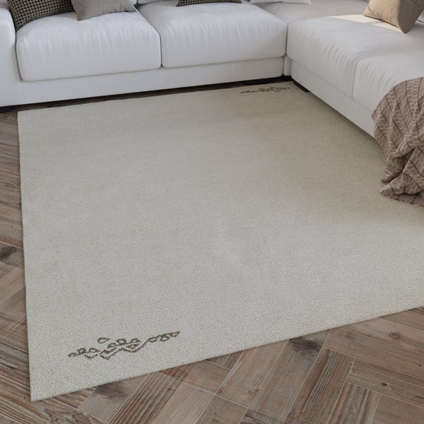 Beiger Kurzflorteppich mit dezenten Ornamenten in den Ecken, liegend auf Parkettboden vor einer weißen Couch in einem hellen Wohnzimmer.