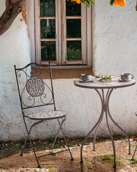 Gartenszene mit Tisch und Stuhl aus Metall mit Mosaikmuster sowie zwei Tassen