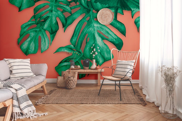 Fototapete mit großen Monstera-Blättern in einem hellen Wohnzimmer mit Holzmöbeln, Jute-Teppich und Parkettboden im Fischgrätmuster.
