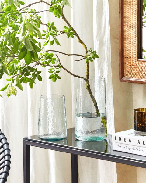 Zwei strukturierte Glasvasen auf einem Tisch mit einem Zweig in einer Vase.
