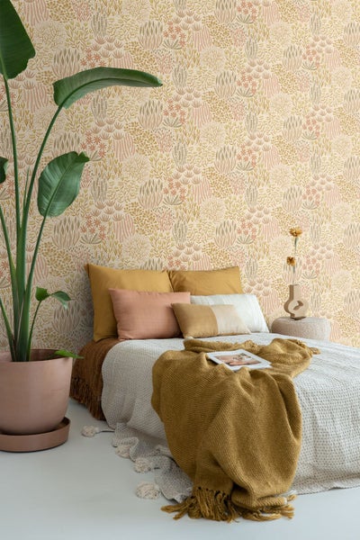 Gemütliches Schlafzimmer mit floral gemusterter Tapete in warmen Tönen, einem Bett mit Strickdecke und einer großen Zimmerpflanze in einem Topf.