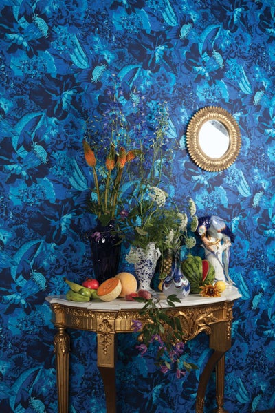 Schlafzimmer mit blau gemusterter Tapete, Bett mit Kissen und Nachttischlampe