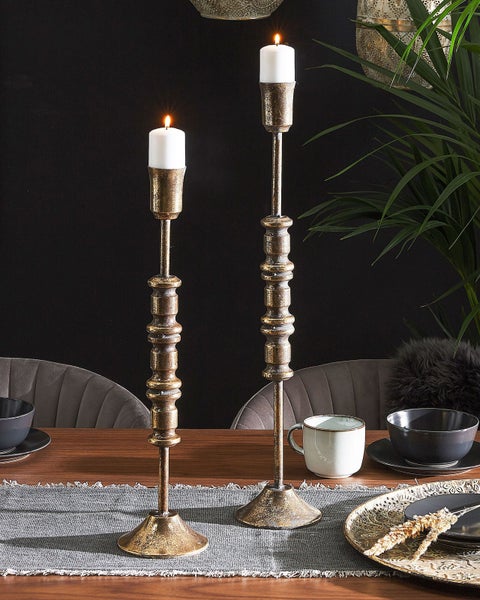 Dekoratives Stillleben mit zwei goldenen Kerzenständern und brennenden Kerzen auf einem gedeckten Tisch.