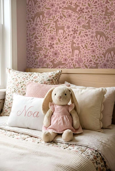 Kinderzimmer mit Tapete mit Rehmotiv und Blumenmuster, dekoriert mit Kuscheltier und Zierkissen auf einem Bett.